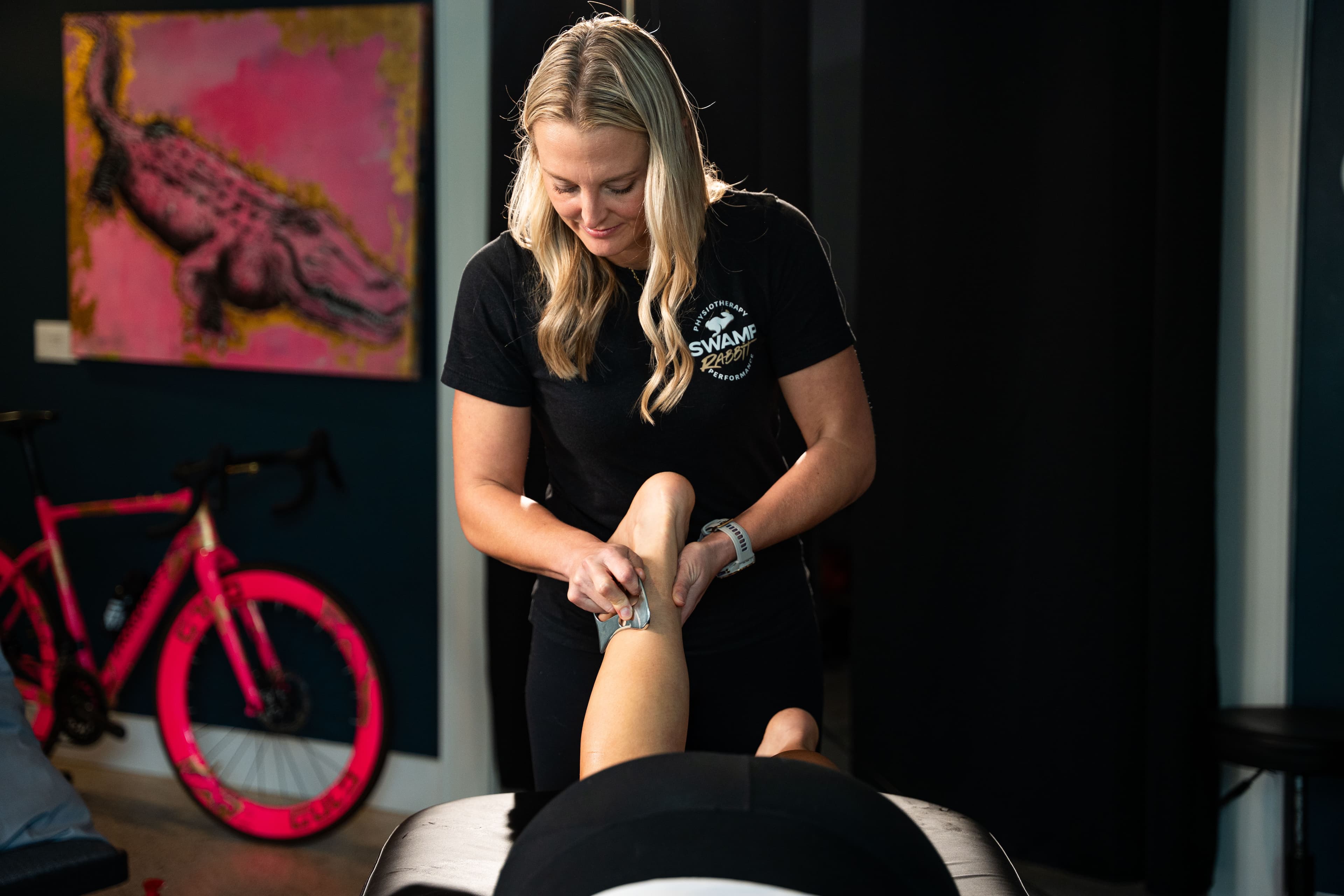 Massage therapist performing instrument-assisted scraping on a patient's lower leg at Swamp Rabbit Physiotherapy in Greenville, SC